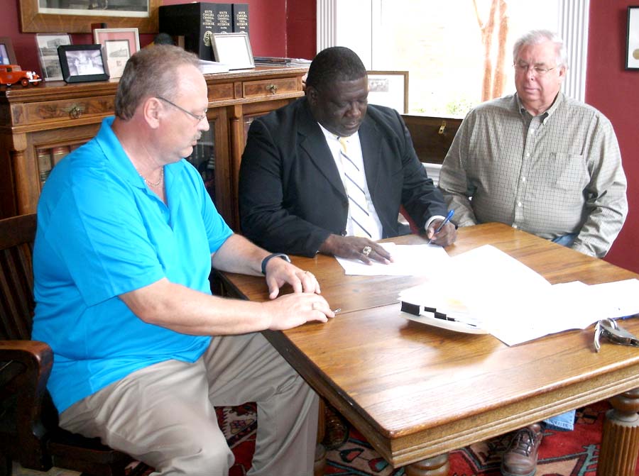 DILLON COUNTY COUNCIL CHAIRMAN Archie Scott (center) signs the paperwork transferring the property for Inland Port Dillon to the South Carolina Ports Authority as landowners Bill Coward (left) and Cullen Bryant (right) look on. Prior to this signing, they signed their property over to the county for the purpose of locating the inland port. The signing took place at the offices of LeGette & Berry. (Photo by Betsy Finklea/The Dillon Herald)